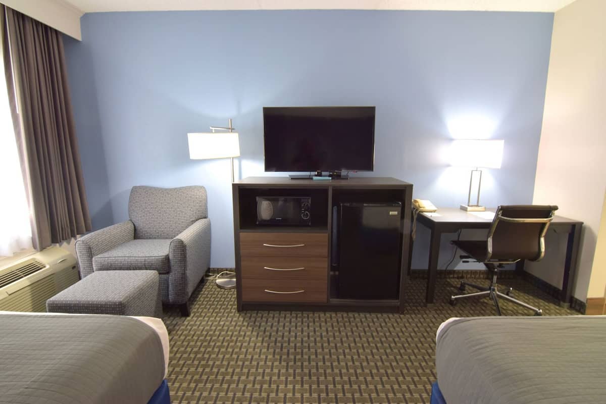 A hotel room with a sofa, a desk with a computer, a television, and a refrigerator.