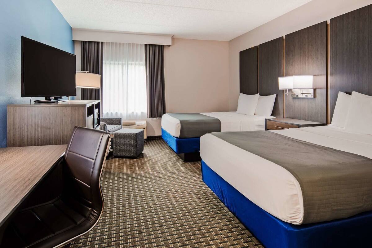A hotel room with a bed, a desk, a chair, a TV, and a window with curtains.