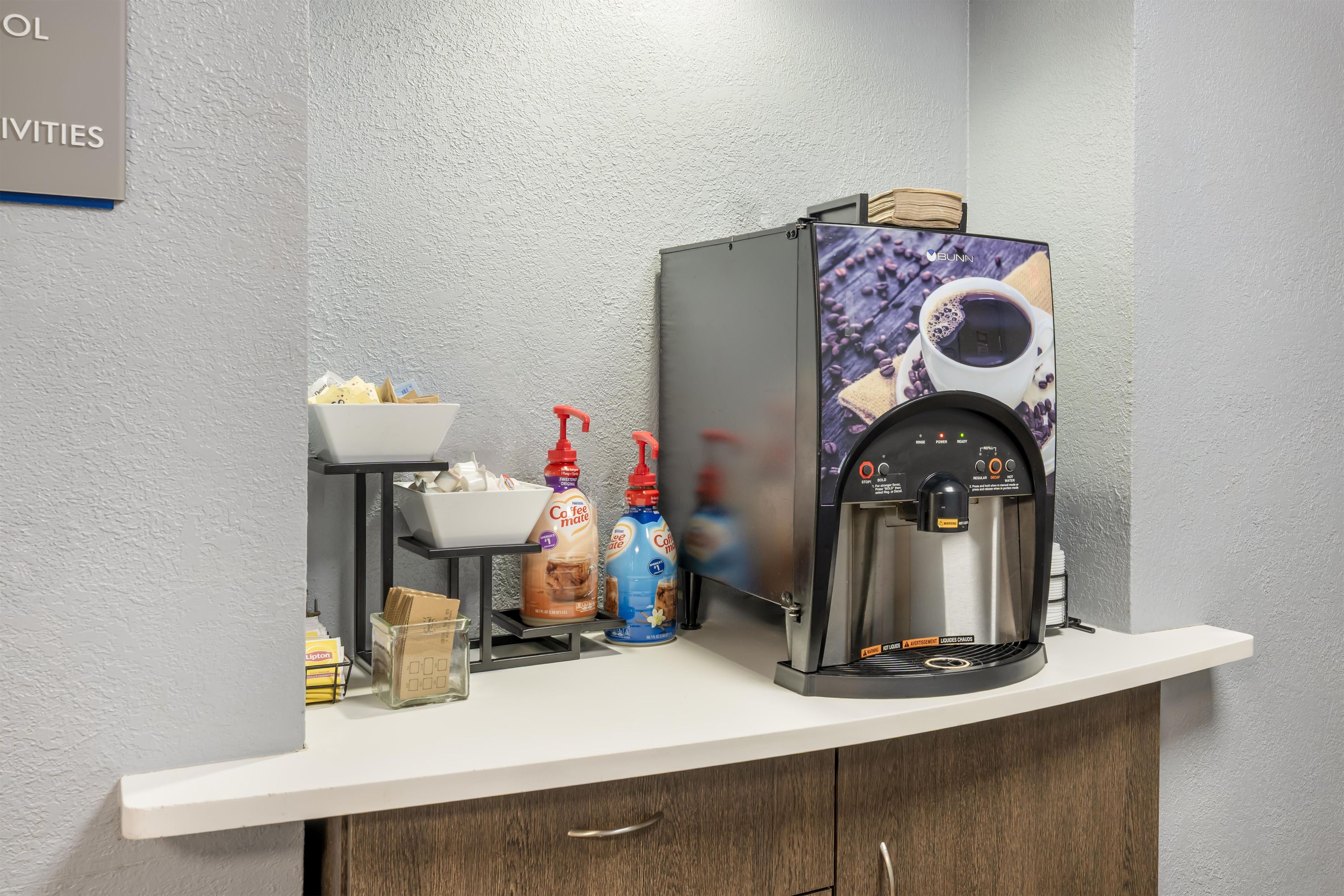 En kaffestation med kaffemaskine, dispensere til mælk og fløde samt en skål med sukker.