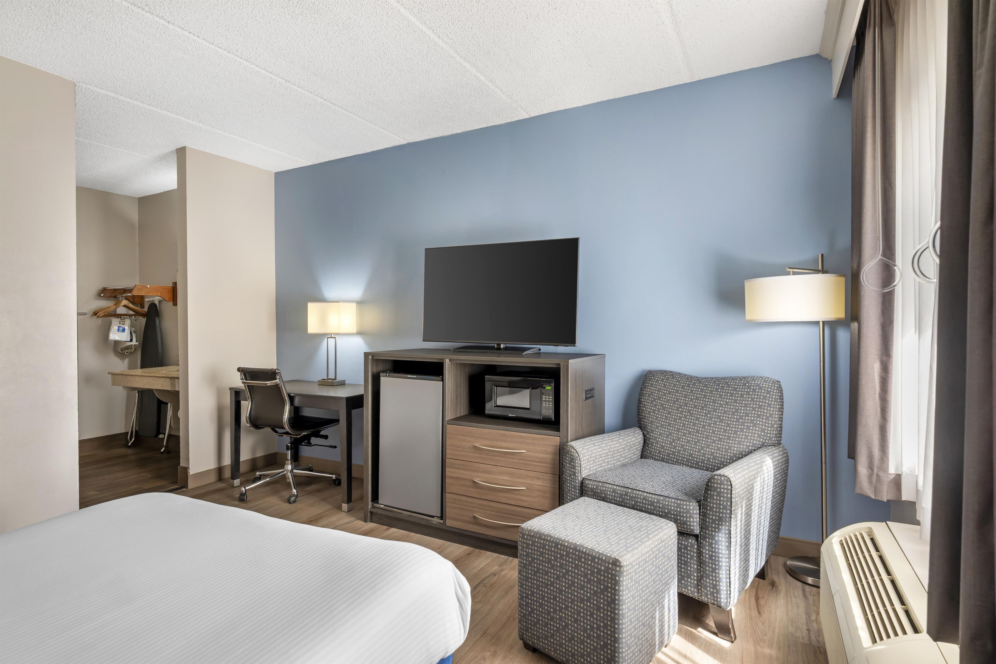 Ett hotellrum med en säng, ett skrivbord, en stol, en tv och ett litet pentry.