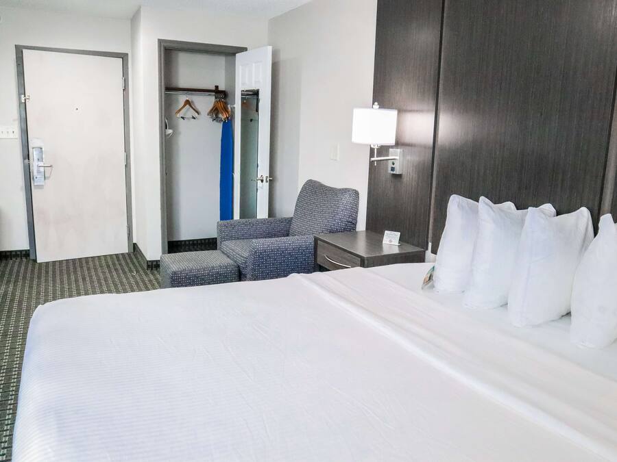 A hotel room with a large bed, a desk with a lamp, a chair, a wardrobe, and a bathroom visible through an open door.