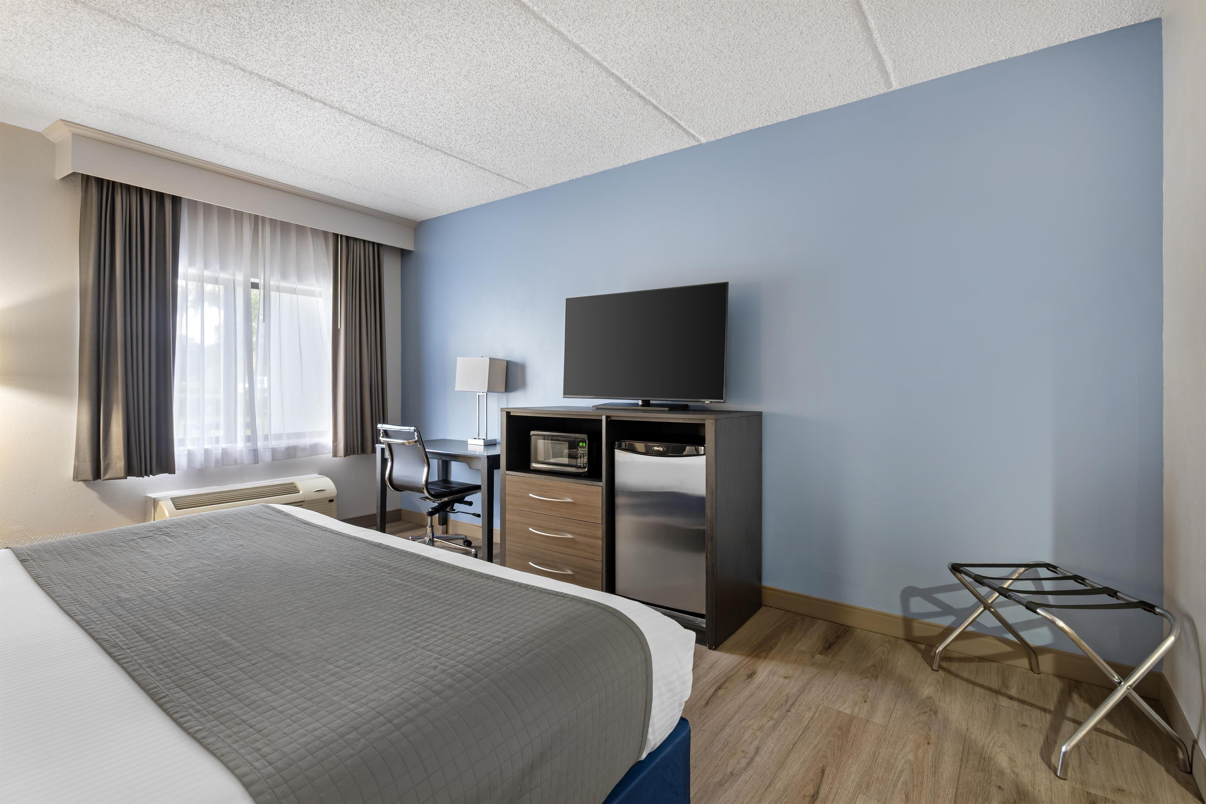 Ein Hotelzimmer mit einem Bett, einem Schreibtisch mit Stuhl, einem Flachbildfernseher, einer Mikrowelle und einem kleinen Tisch mit Stuhl.