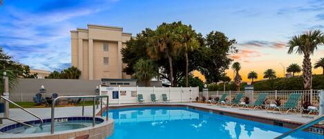 A swimming pool with lounge chairs, a hot tub, and a building in the background.
