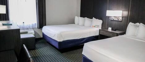 A hotel room with two beds, a desk, a chair, a nightstand, and a window with curtains.