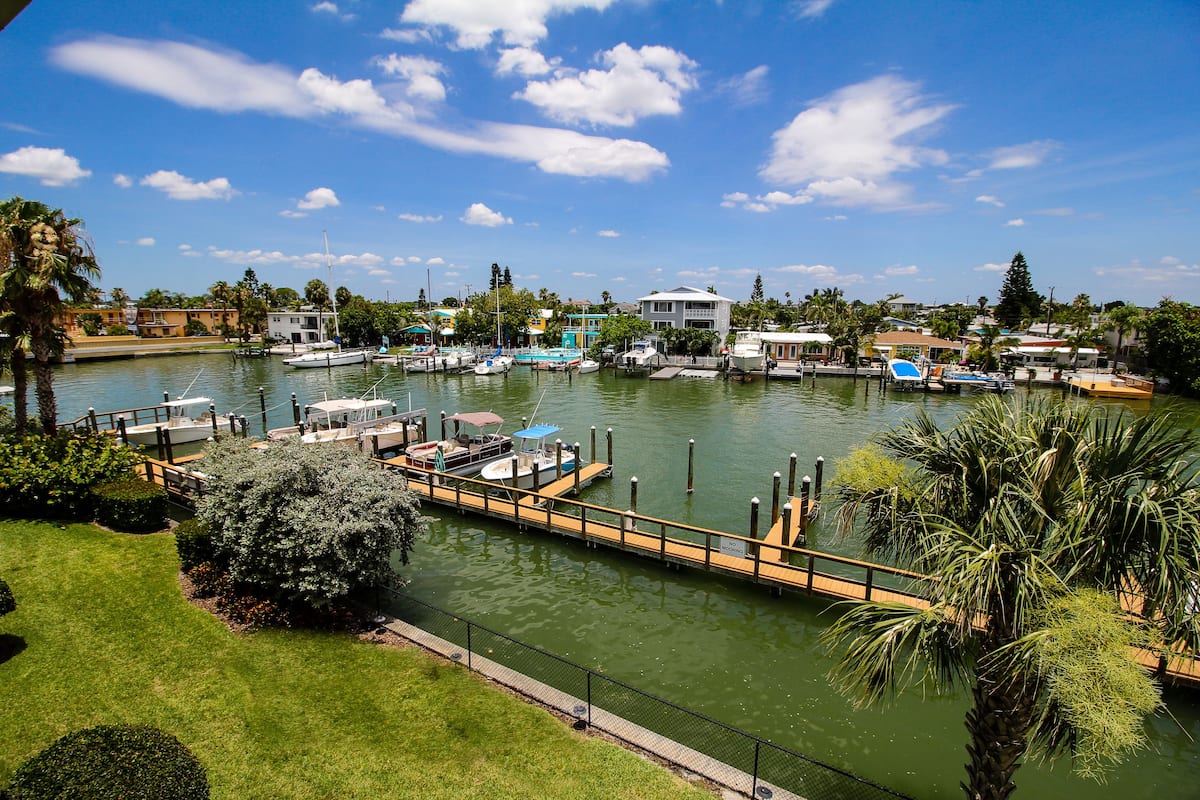 Un puerto deportivo con barcos amarrados, una zona verde y un edificio grande al fondo.