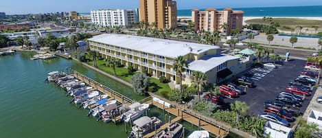 Un puerto deportivo con barcos amarrados, un estacionamiento y un hotel de varios pisos con balcones con vista al agua.