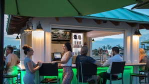 Un área de bar al aire libre con mostrador, sillas y vista a la playa.