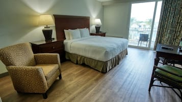 A hotel room with a bed, two nightstands, a chair, a desk, and a view of the outdoors through a large window.