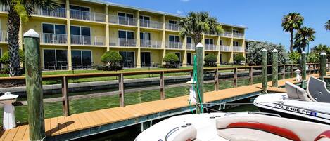 Un hotel frente al agua con un muelle, un bote y un edificio con balcones.