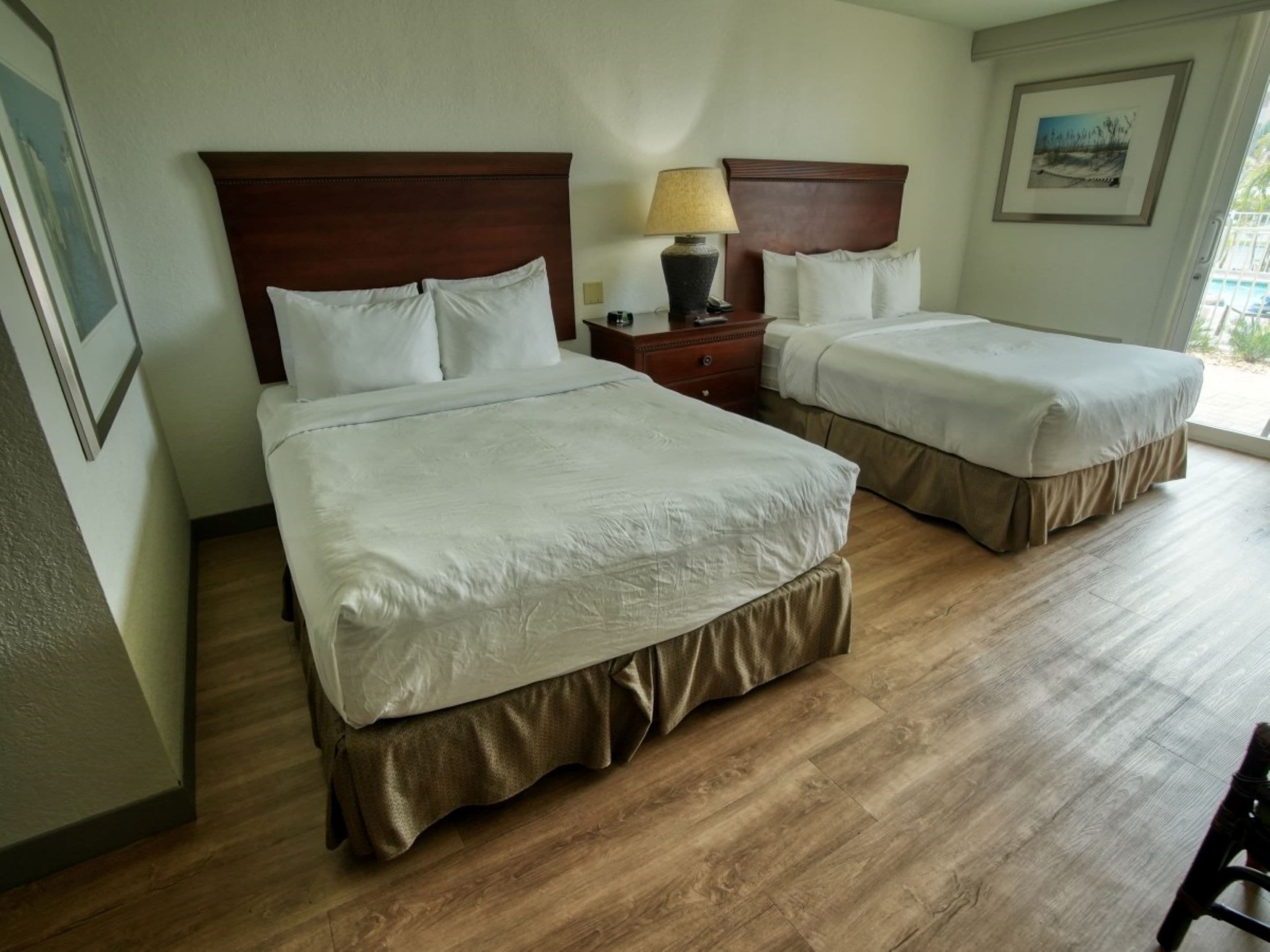 Une chambre d’hôtel avec deux lits, un plancher en bois et une table de chevet avec une lampe.