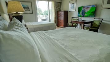 Ein Hotelzimmer mit einem großen Bett, einem Einzelbett, einem Schreibtisch mit Stuhl, einem Schminktisch und einem Fernseher. Ein Fenster mit Vorhängen vorhanden.
