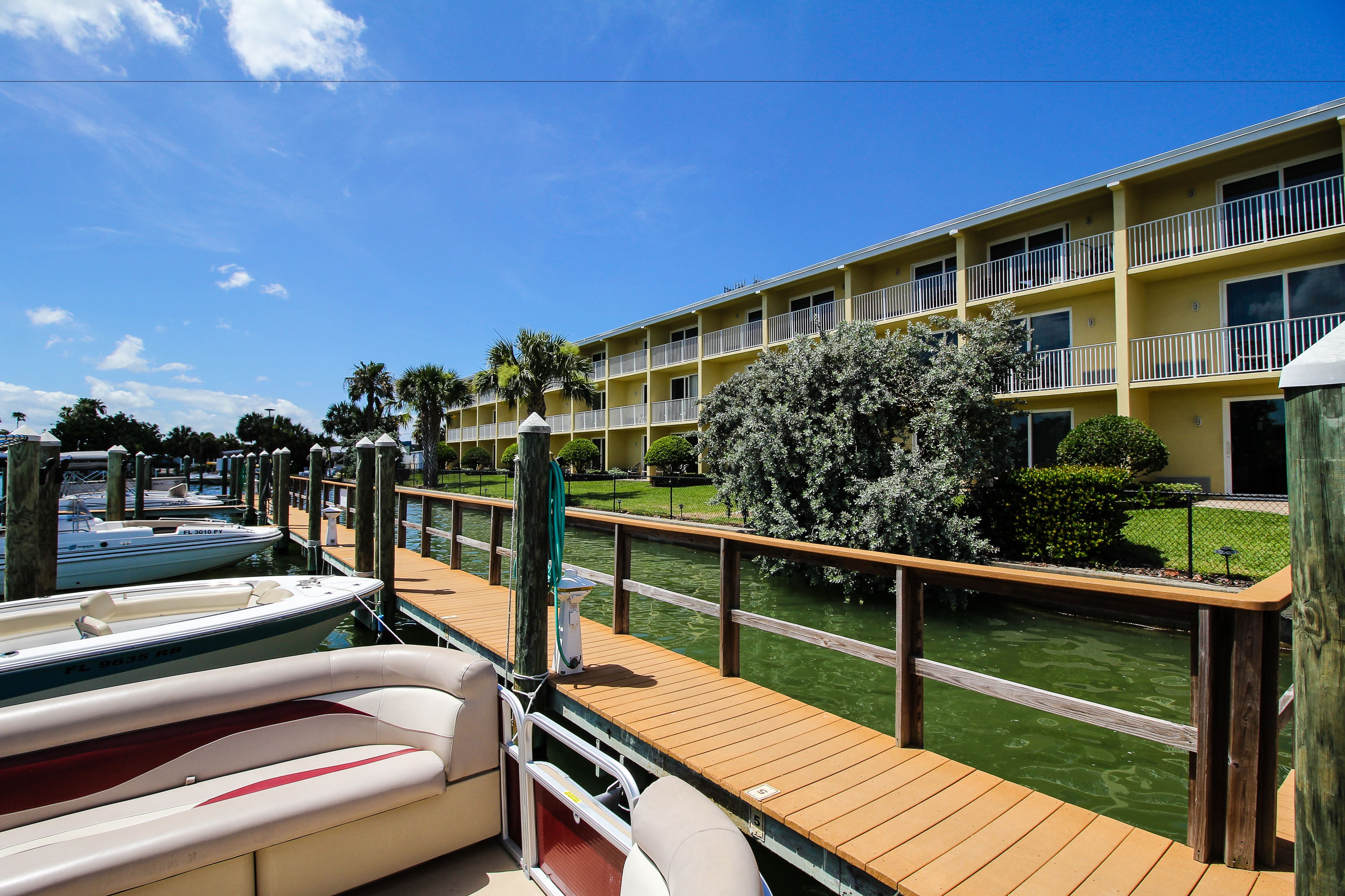 A wooden dock with boats, a marina, and a yellow building with balconies.