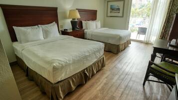 Quarto de hotel com duas camas, uma escrivaninha, uma cadeira e uma janela com vista para palmeiras.
