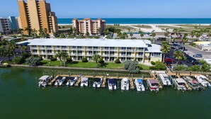 Un puerto deportivo con barcos amarrados, un hotel con techo plano y una playa al fondo.