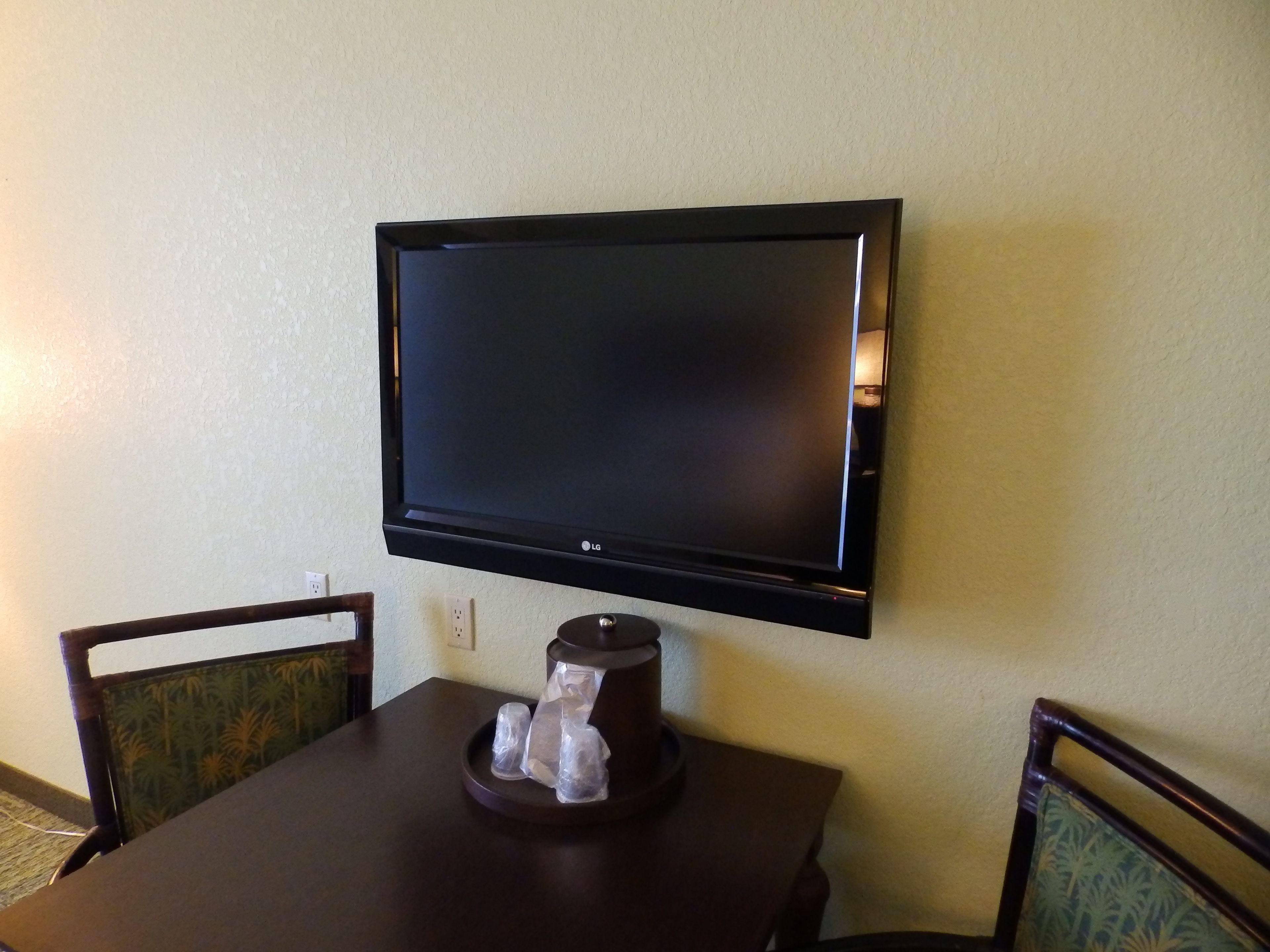 Un televisor de pantalla plana montado en la pared sobre una mesa de madera oscura con sillas.