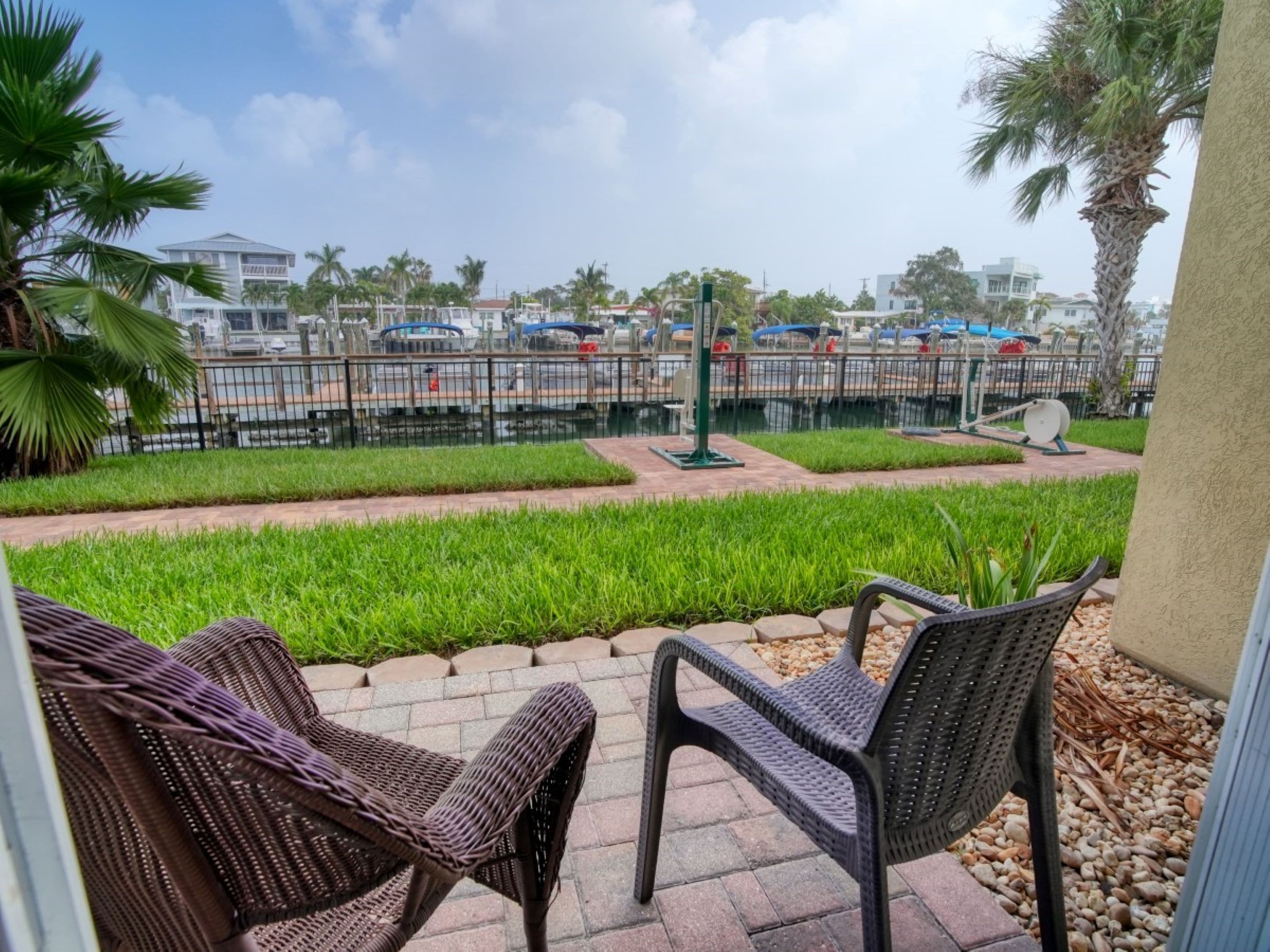 A patio area with wicker chairs and a view of a parking lot with cars and a water feature.