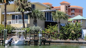 Una propiedad frente al agua con muelle para barcos, palmeras y un edificio con balcón.