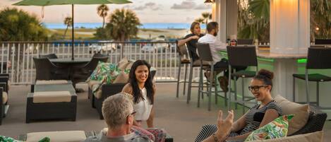 An outdoor seating area with wicker furniture, a bar, and a view of the beach.