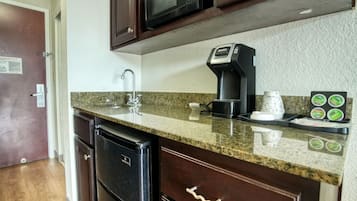 Una cocina con microondas, cafetera y soporte para cápsulas de café.