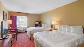 A hotel room with two beds, a desk with a television, a bookshelf, and a window with curtains.
