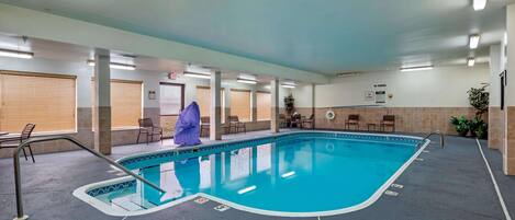 An indoor swimming pool with a tiled floor, a pool ladder, and a few chairs around the pool area.