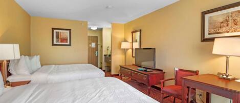 Habitación de hotel con dos camas, un escritorio, una silla, un televisor y un espejo.