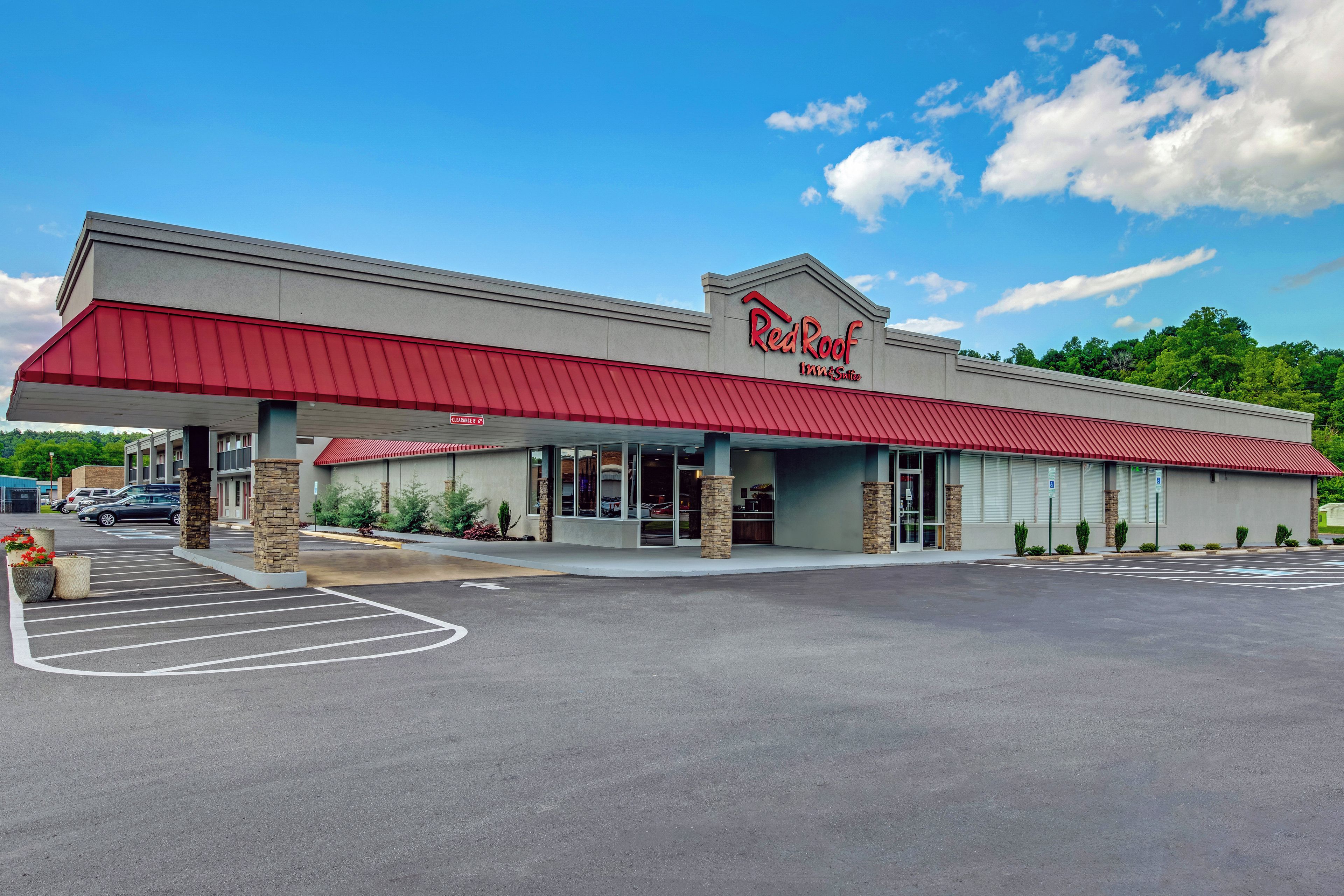 A Red Roof Inn & Suites with a red awning, a parking lot, and a clear sky.