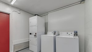 A laundry room with stacked washer and dryer units, a control panel, and a red door. - Red Roof Inn & Suites Wilkesboro (Wilkesboro)