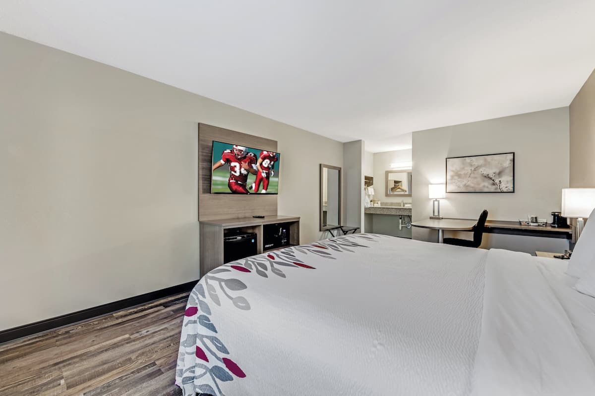 Une chambre d’hôtel avec un grand lit, un téléviseur à écran plat fixé au mur, un bureau avec une chaise, une petite table et un miroir.
