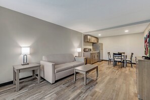 A modern living room with a sofa, coffee table, and side tables, a kitchenette with cabinets and appliances, and a dining area with chairs and a table. - Red Roof Inn & Suites Wilkesboro (Wilkesboro)