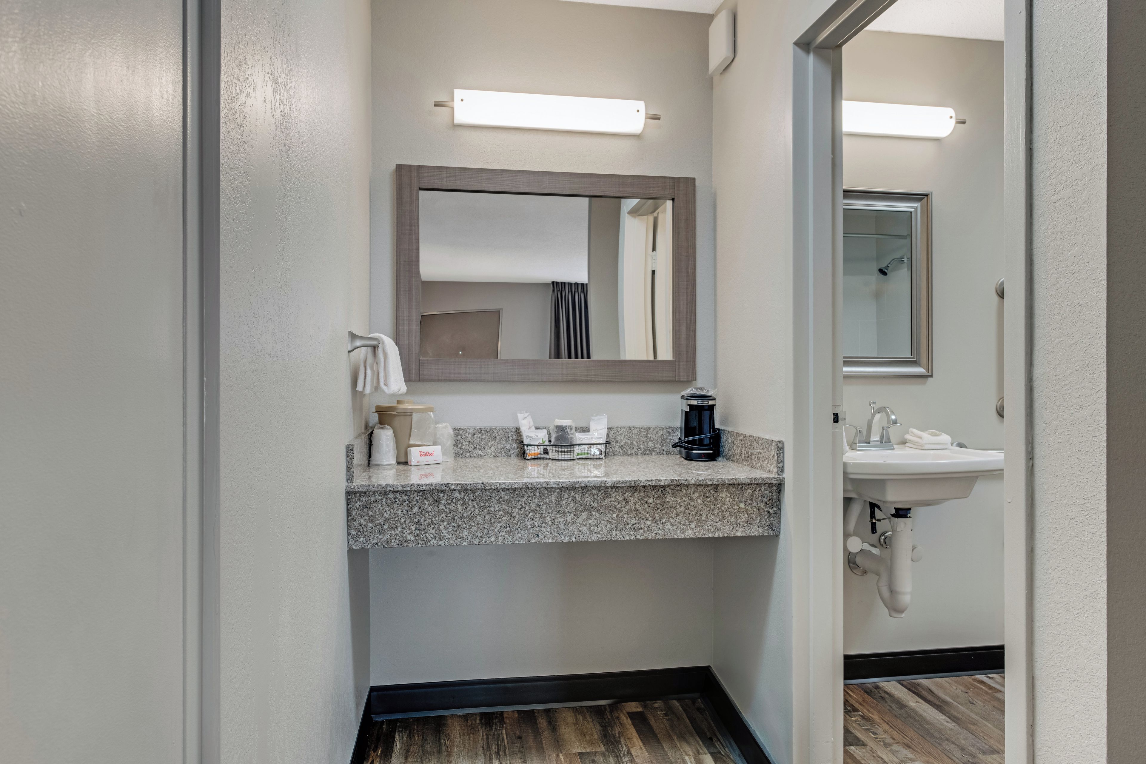 A hotel bathroom with a granite countertop, a coffee maker, a sink, and a mirror.