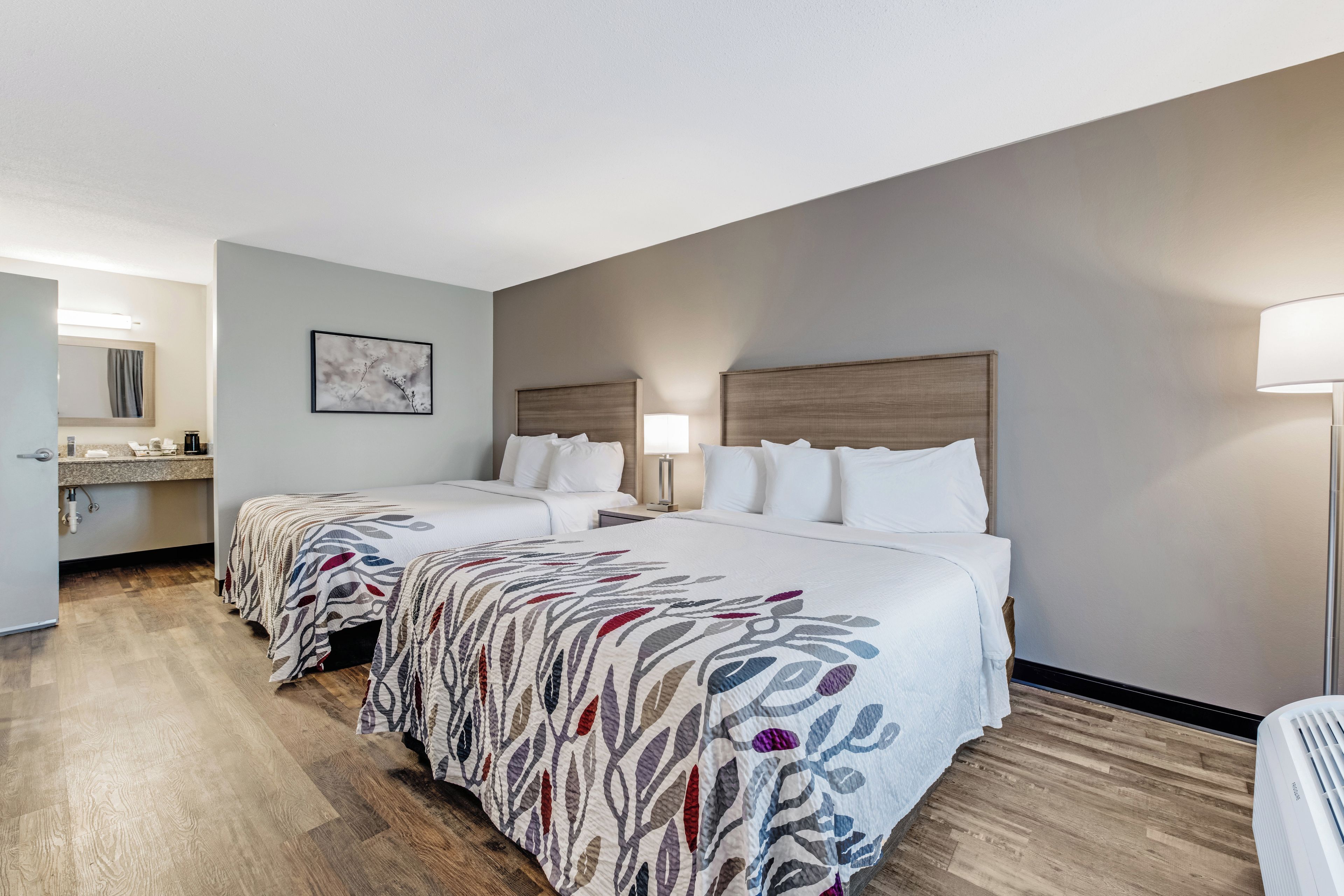 A hotel room with two beds, a bathroom, and a kitchenette.