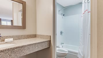 A bathroom with a granite countertop, a toilet, a shower with a white curtain, and a mirror.