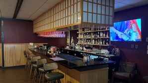 A bar area with a long counter, bar stools, shelves with bottles, and a television screen. - Red Roof Inn & Suites Wilkesboro (Wilkesboro)
