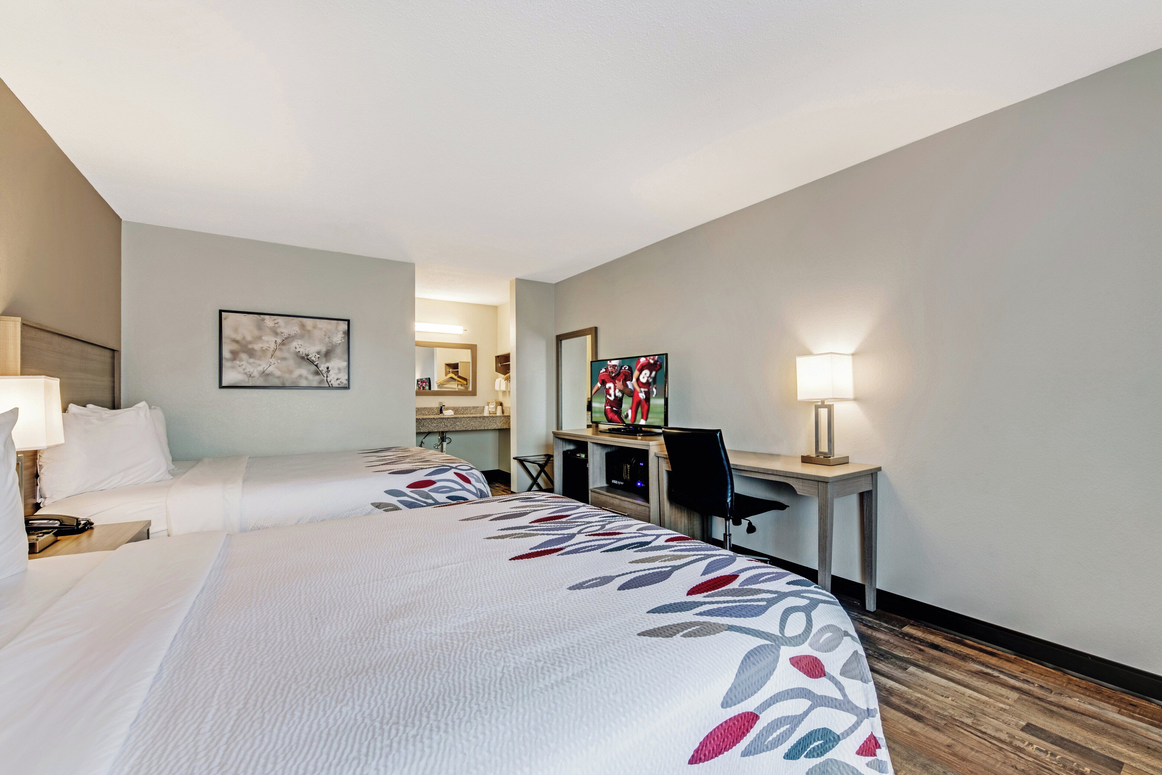 Une chambre d’hôtel avec deux lits, un bureau, une chaise, une télévision et une lampe.