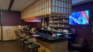 A bar area with a long counter, bar stools, shelves with bottles, and a television screen.