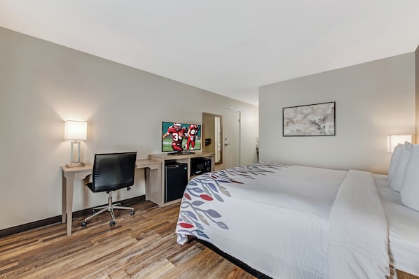 A hotel room with a bed, desk, chair, television, and artwork on the walls.