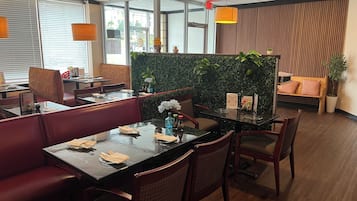 Ein modernes Restaurant mit Glastischen, gepolsterten Sitzbereichen und einer grünen Wand mit Pflanzen.