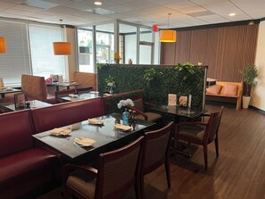 A modern restaurant with glass tables, cushioned booths, and a green wall with plants. - Red Roof Inn & Suites Wilkesboro (Wilkesboro)