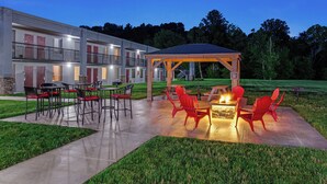 A hotel with a covered outdoor seating area, a fire pit, and a well-maintained lawn.