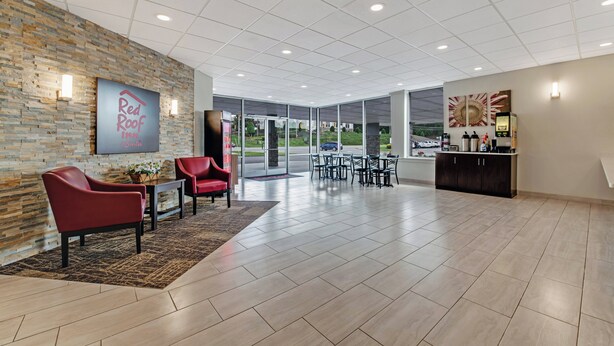 A spacious lobby with a Red Roof Inn sign, a reception desk, and a seating area with red chairs.