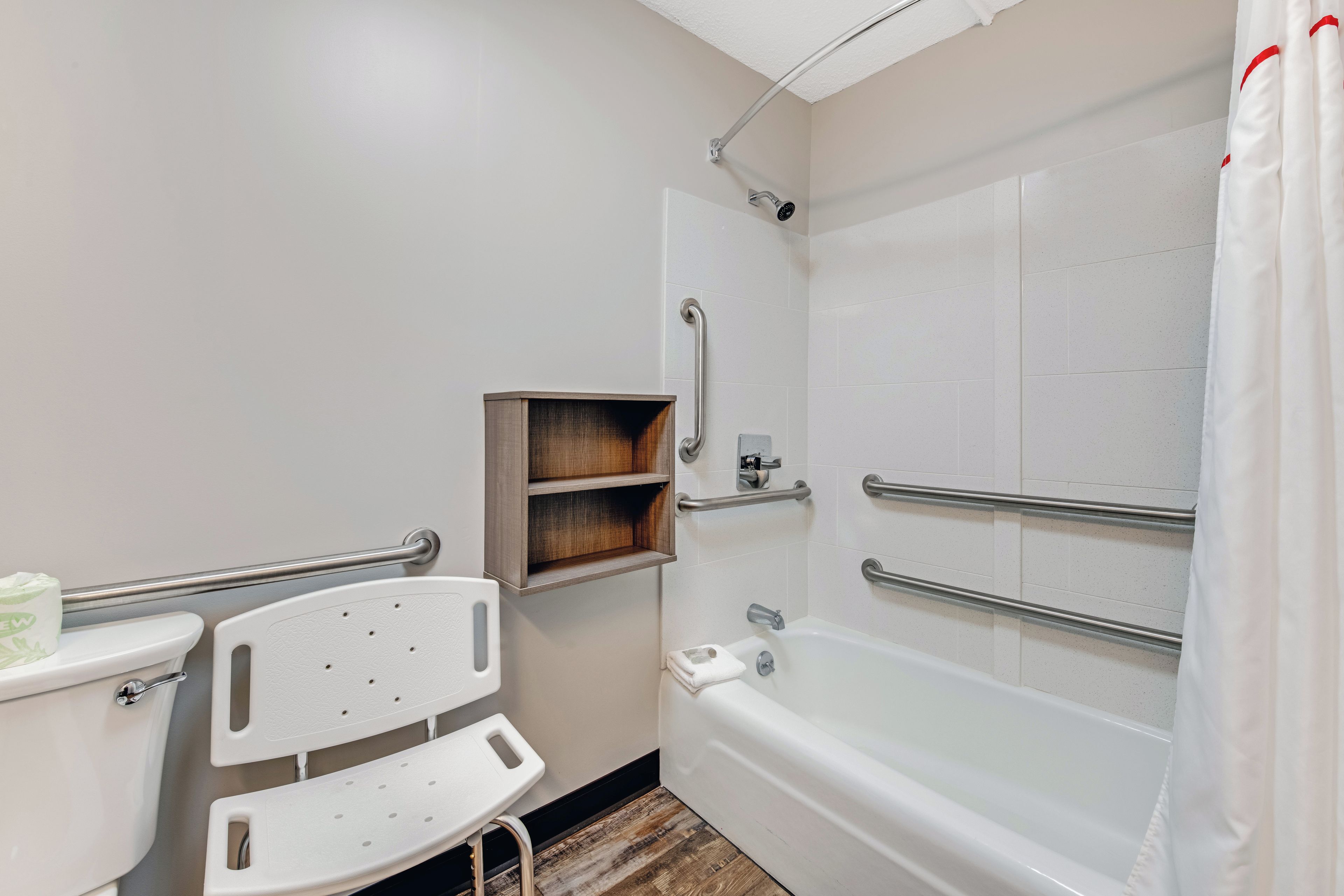 Un baño con inodoro blanco, ducha blanca con puerta de vidrio y un estante de madera.