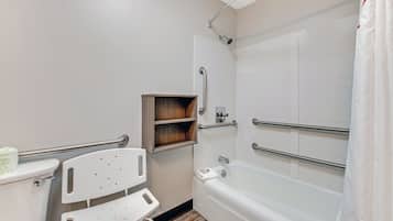 Un baño con inodoro blanco, ducha blanca con puerta de vidrio y un estante de madera.