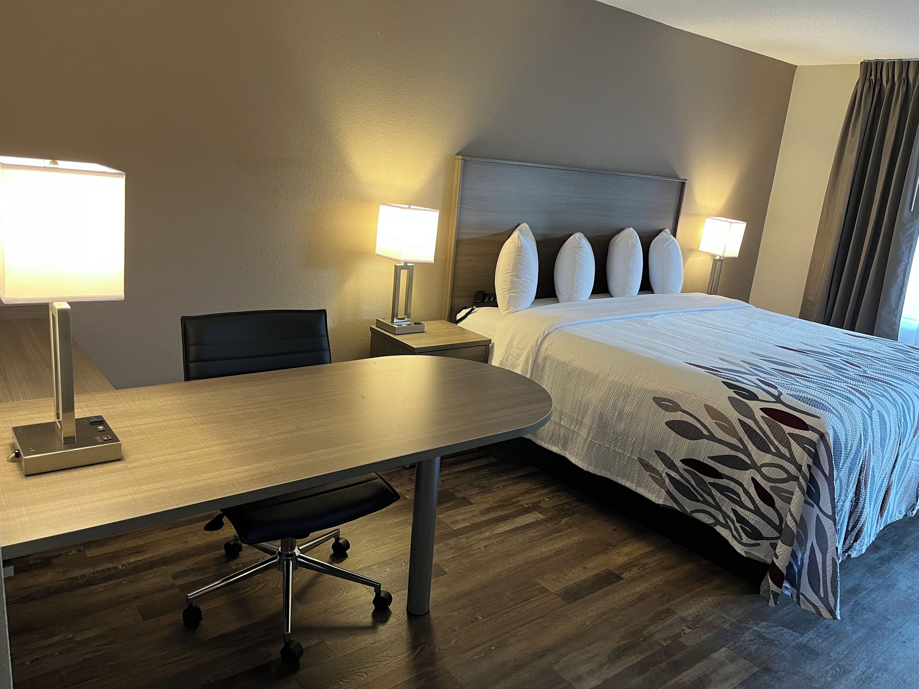 A hotel room with a bed, two bedside lamps, a desk with a chair, and a telephone.