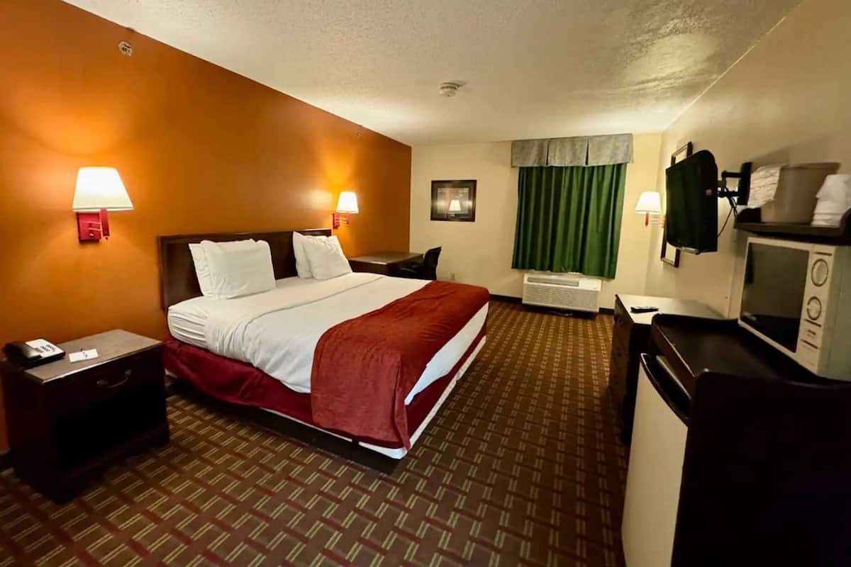 Une chambre d’hôtel équipée d’un lit, de tables de chevet, d’un bureau, d’un four à micro-ondes et d’une fenêtre avec des rideaux.