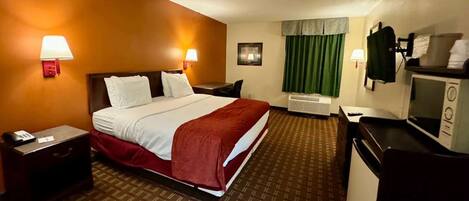A hotel room with a bed, bedside tables, a desk, a microwave, and a window with curtains.