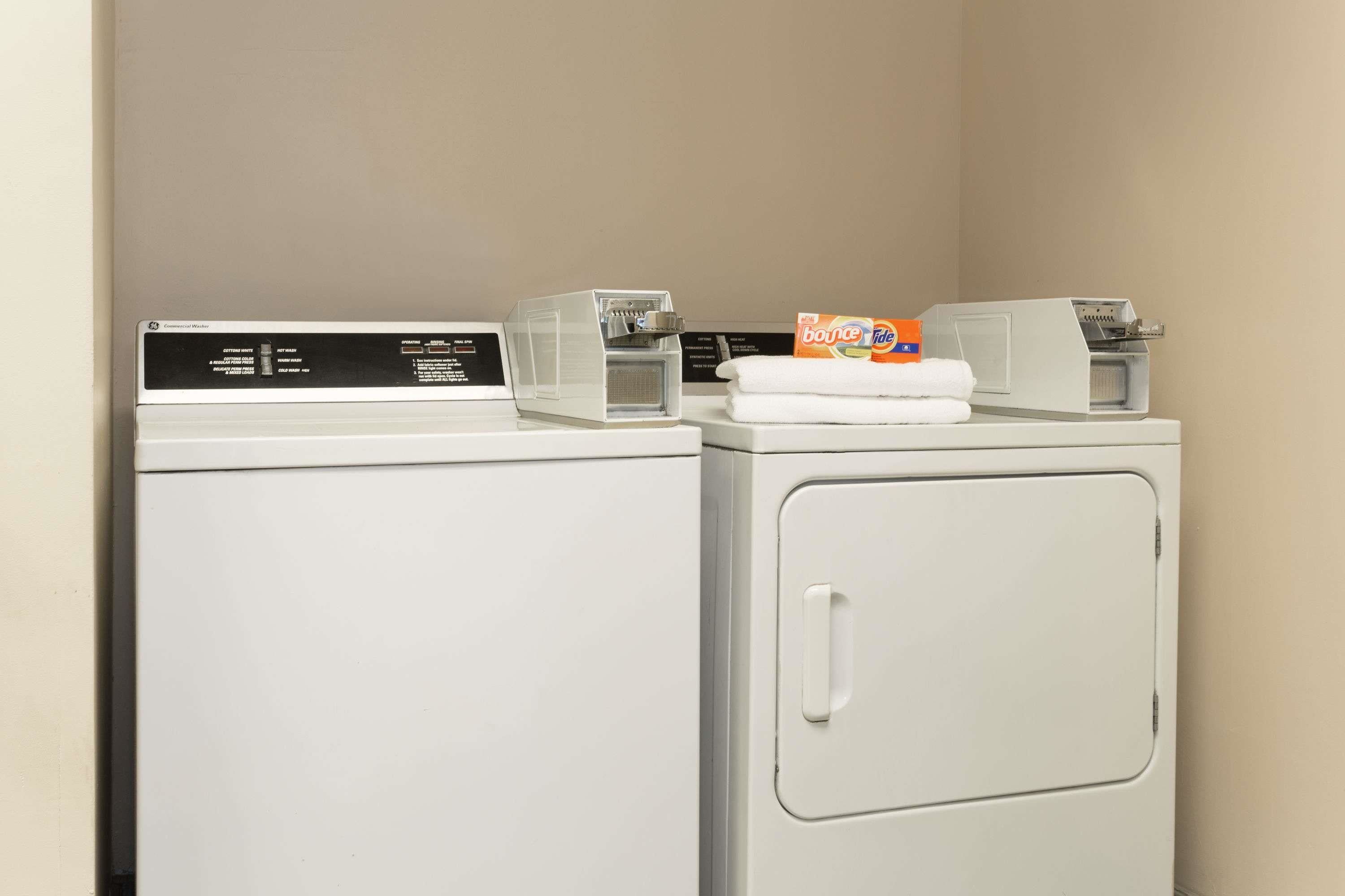 A laundry area with two washing machines and a dryer, a folded towel, and a box of laundry detergent.