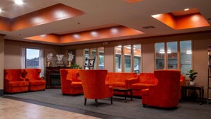 A lobby with orange armchairs, a fireplace, and large windows.