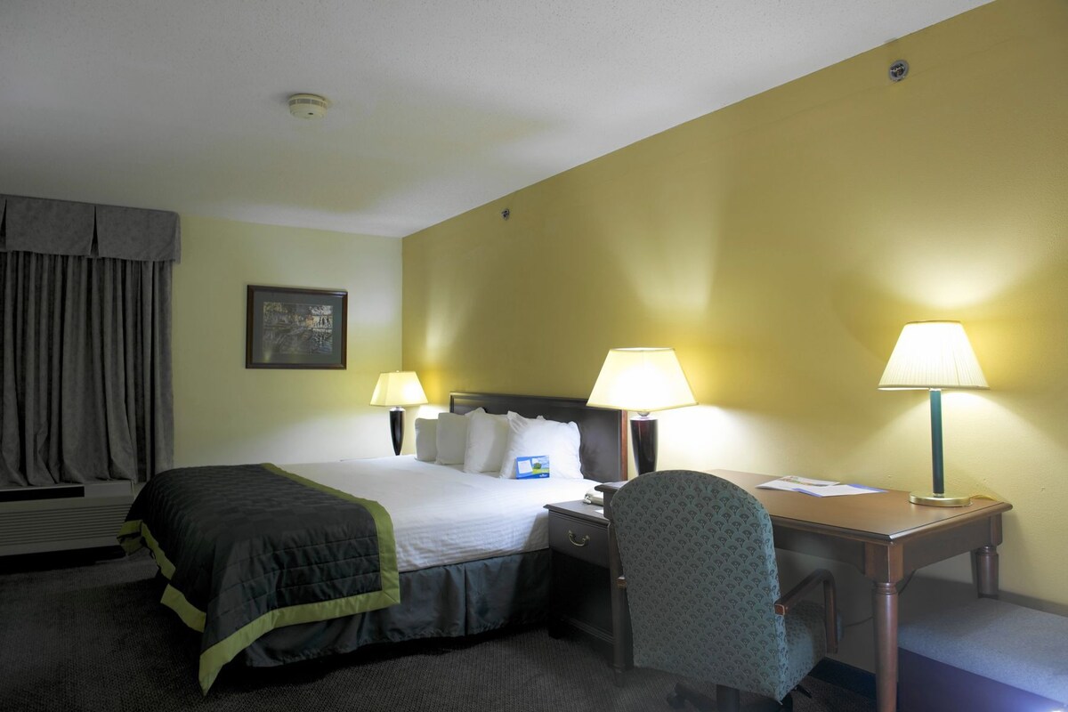 A hotel room with a bed, two bedside lamps, a desk with a chair, a picture on the wall, and a window with curtains.