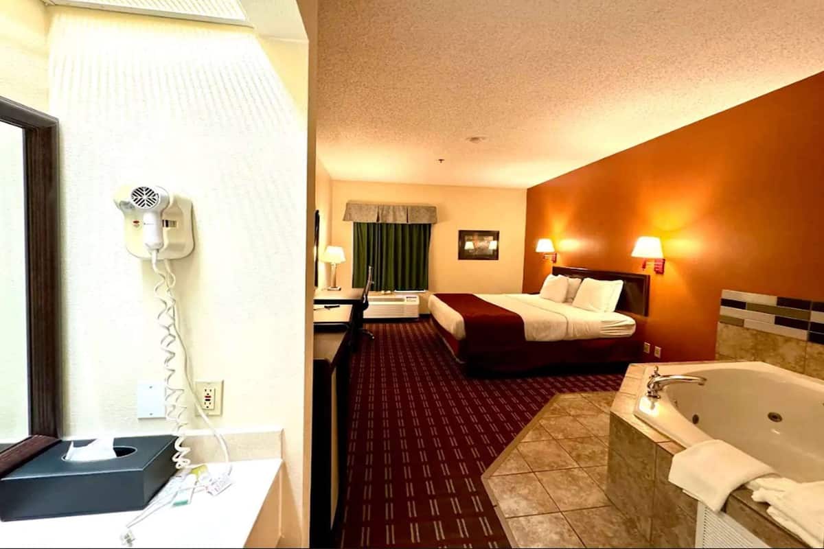 Une chambre d’hôtel comprenant un lit, un bureau, un sèche-cheveux, une salle de bain avec baignoire et une fenêtre avec des rideaux.